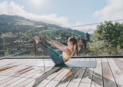 Frau bei Pilatesübungen auf einer Yogamatte auf dem Balkon